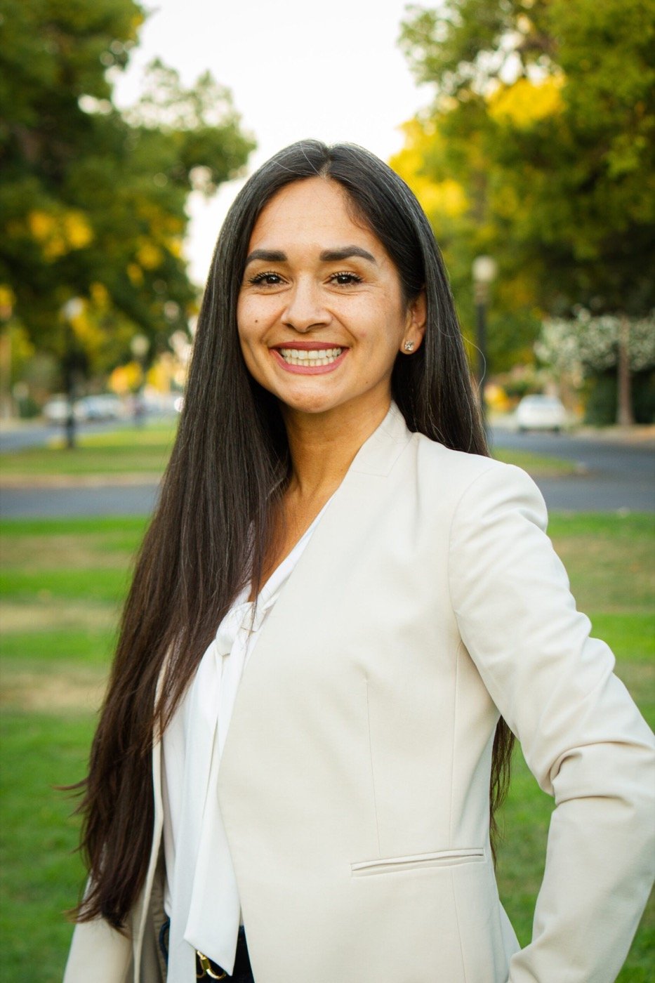 Ariana Martínez Lott smiling outdoors on a tree-lined South Fresno street, wearing a cream blazer